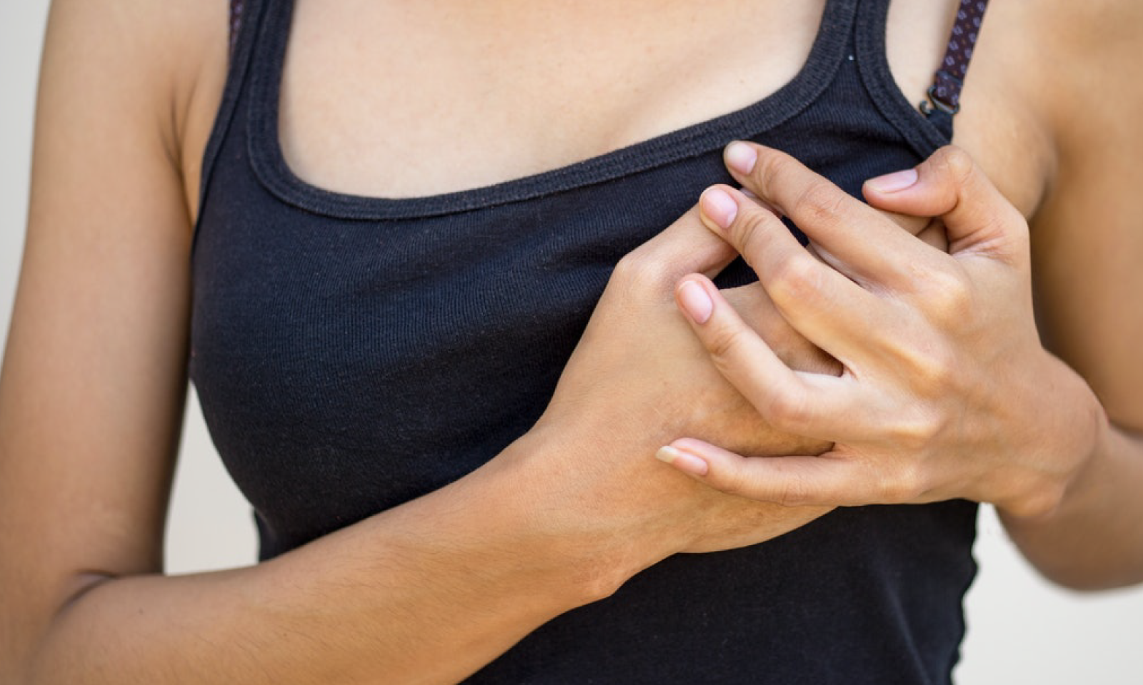 A woman in a black tank top is holding her left breast with both of her hands.