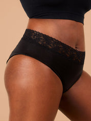 A close-up of a Black woman standing in black period pants with floral lace trim, showcasing the details.